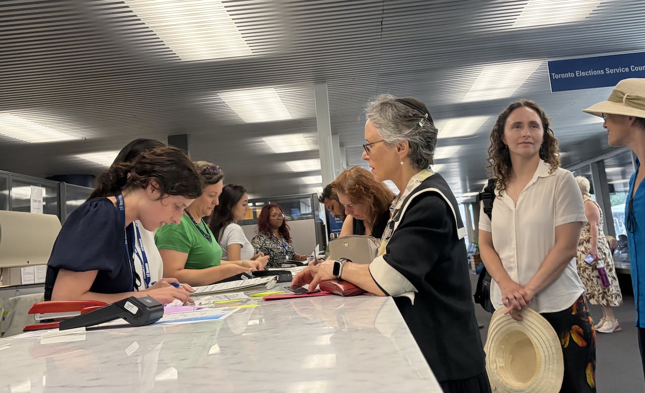 A woman is at a desk speaking with someone.