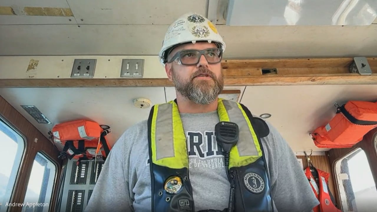 A man in a hard hat and safety vest stands inside a tugboat.
