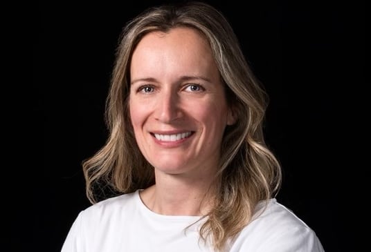 A woman in a white T-shirt stands in front of a black background.