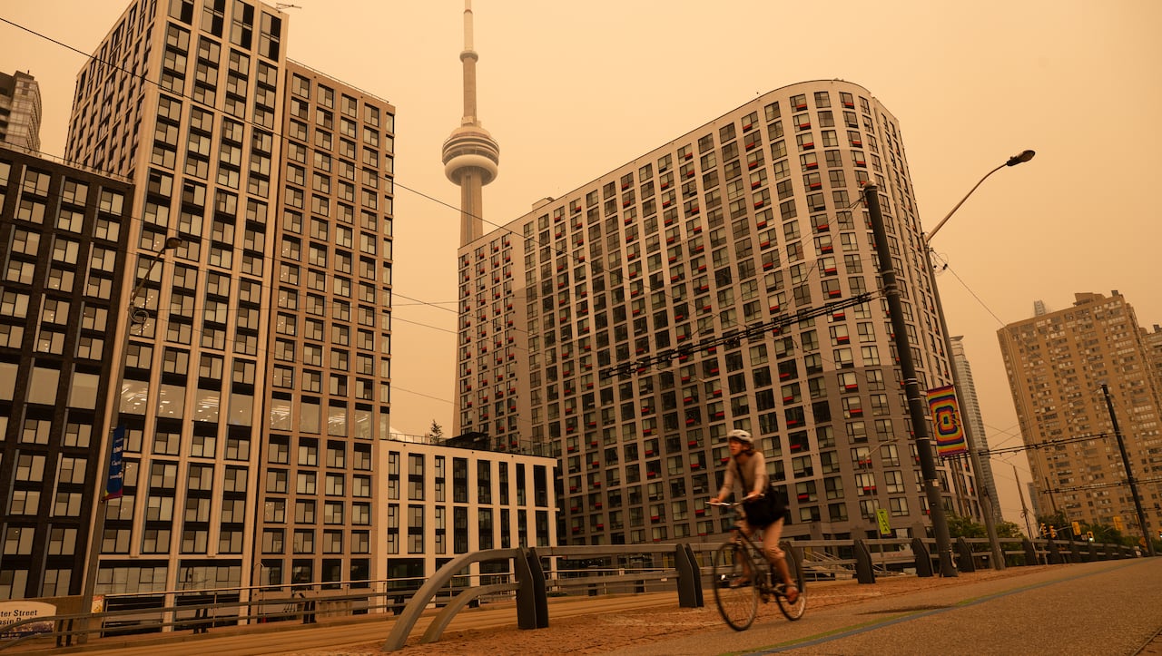 Toronto is shown, with the CN Tower visible, with a thick orange overlay of wildfire smoke tinting the air.