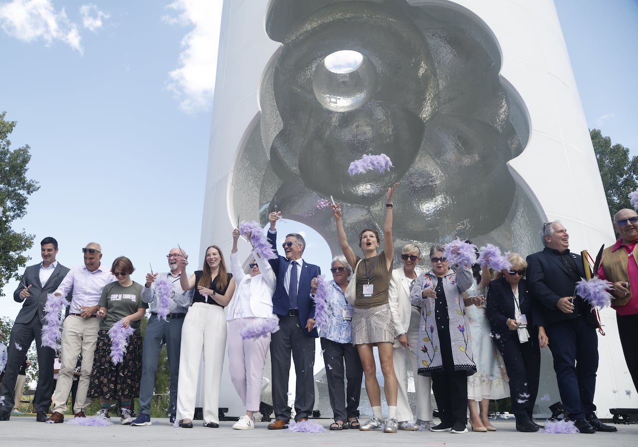 A line of people cheer and celebrate while standing in front of a large white-and-grey monument.