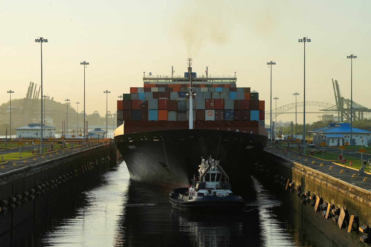 A photo of a container ship waiting in the lock of the Panama Canal, with a smaller pilot vessel on the water behind it.