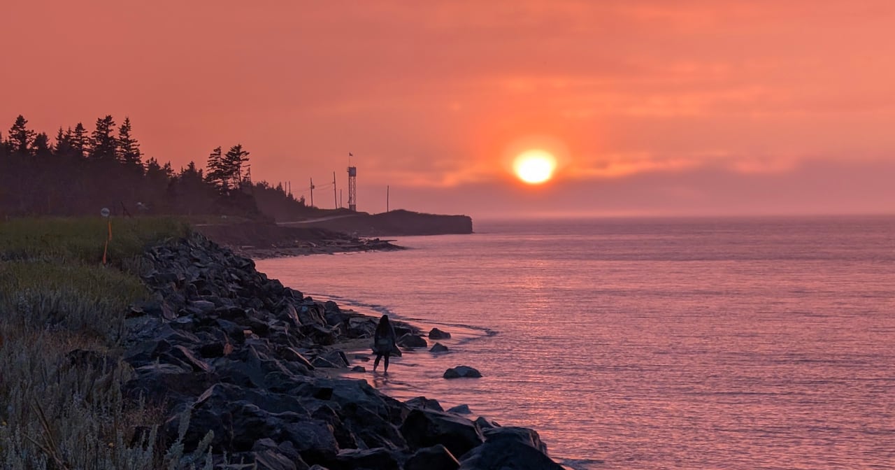 The sun sinks over a bay, turning the water pink and the sky orange.