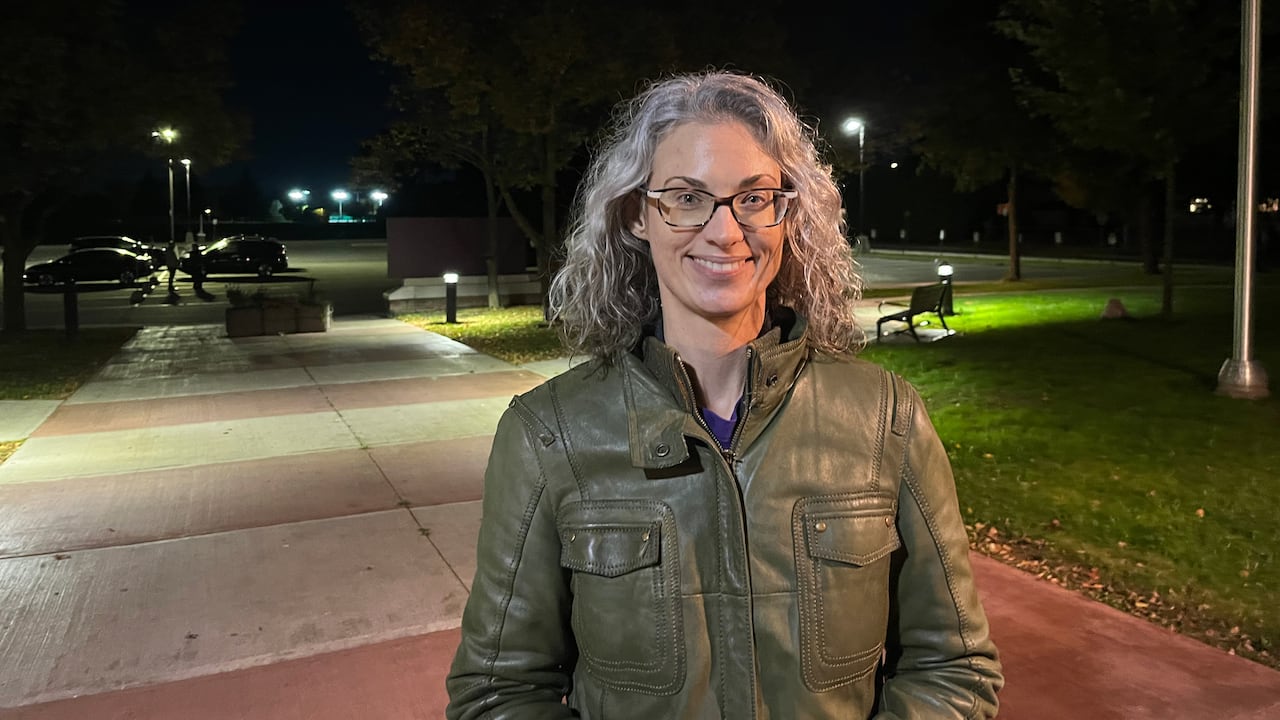 A woman stands outdoors at night and smiles for a photo.