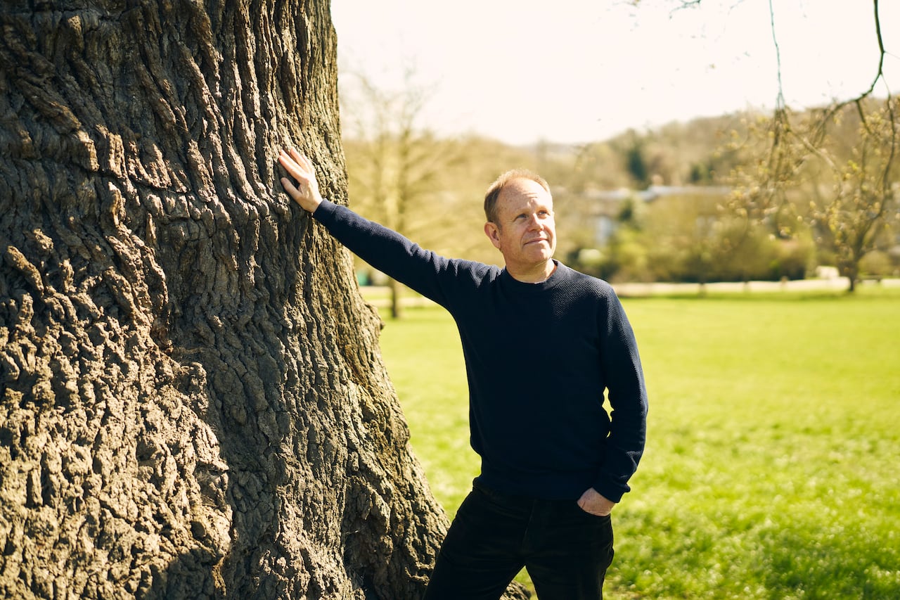 A man in jeans poses for a photo on a rock, holding a camera in one hand.