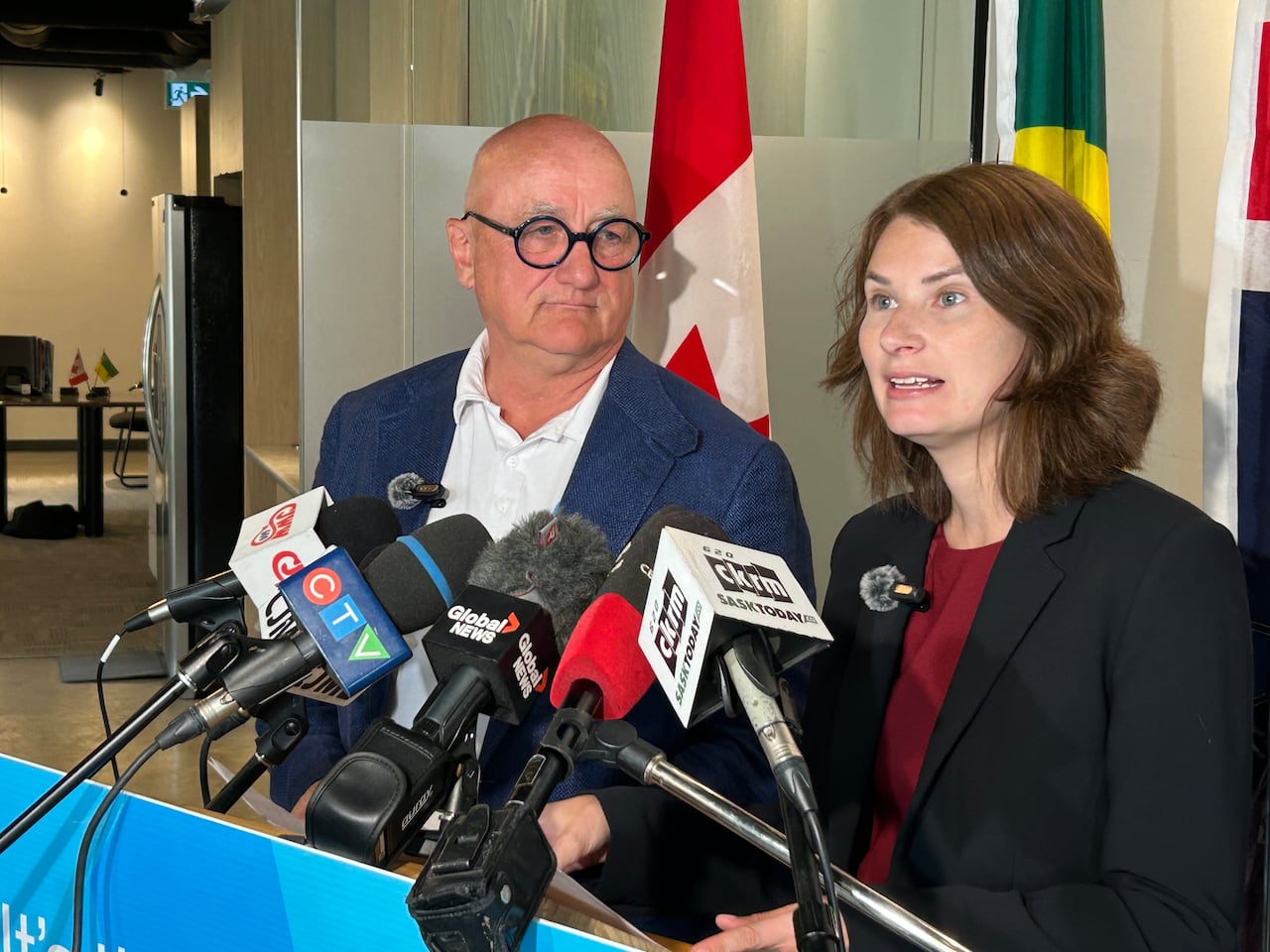 a man and a woman speak at a podium with microphones from media organization attached