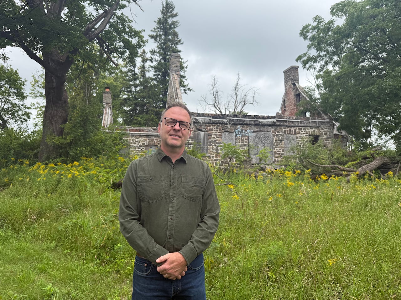 Man in green shirt, stands outside of the Maison Michel Robillard, an 18th century farmhouse.