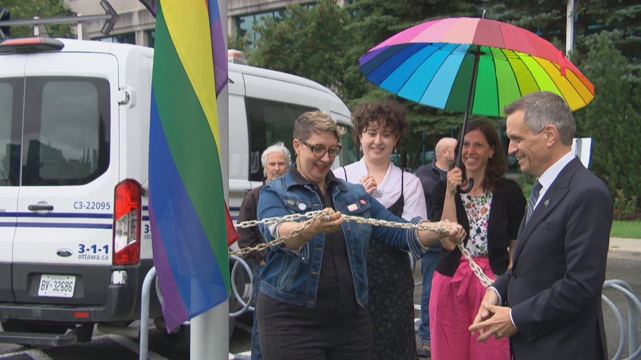 Councillor Ariel Troster and Mayor Mark Sutcliffe pull a chain to raise the Pride flag.