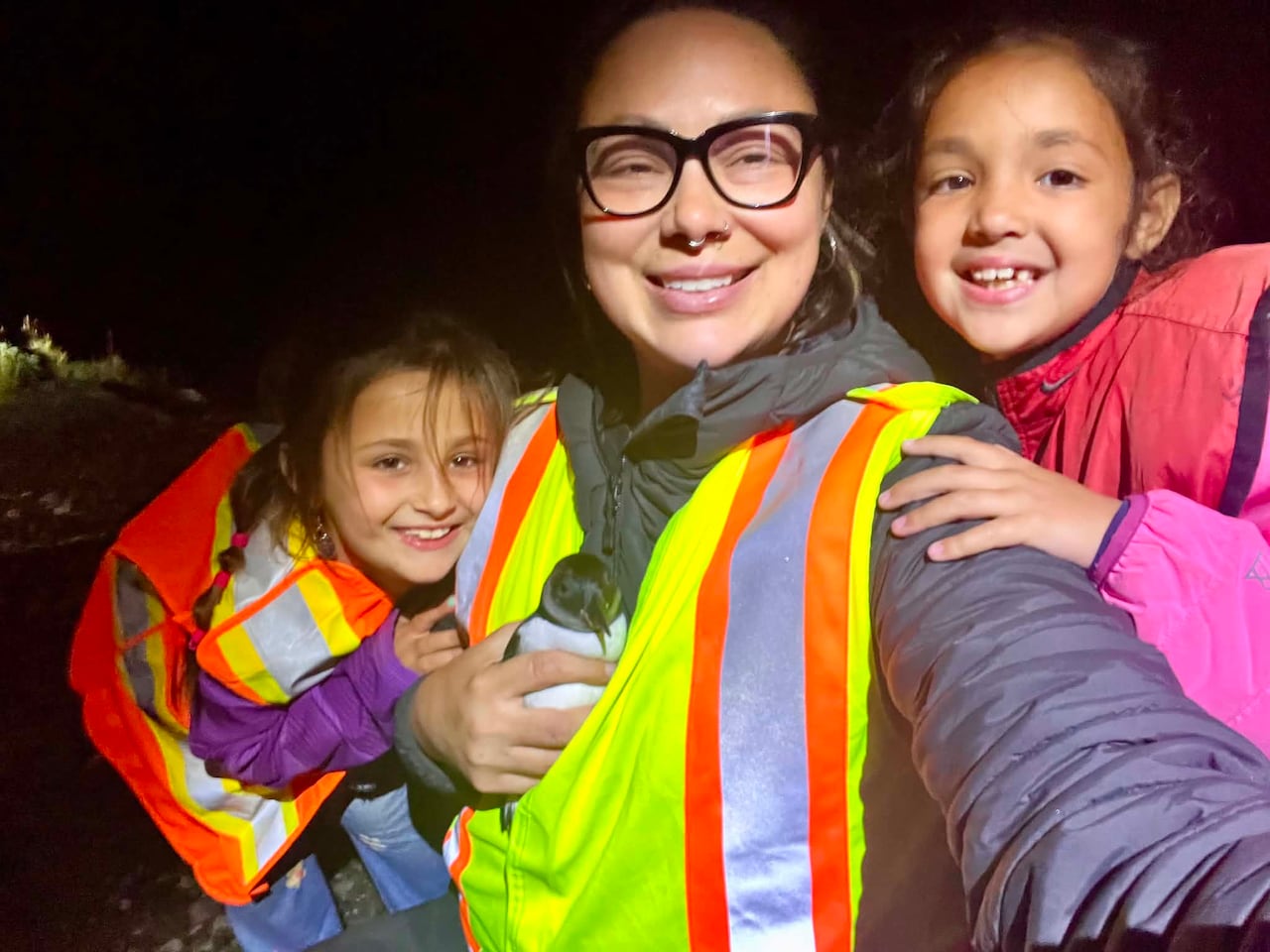 A woman holds a puffin, with two children, all wearing safety vests.