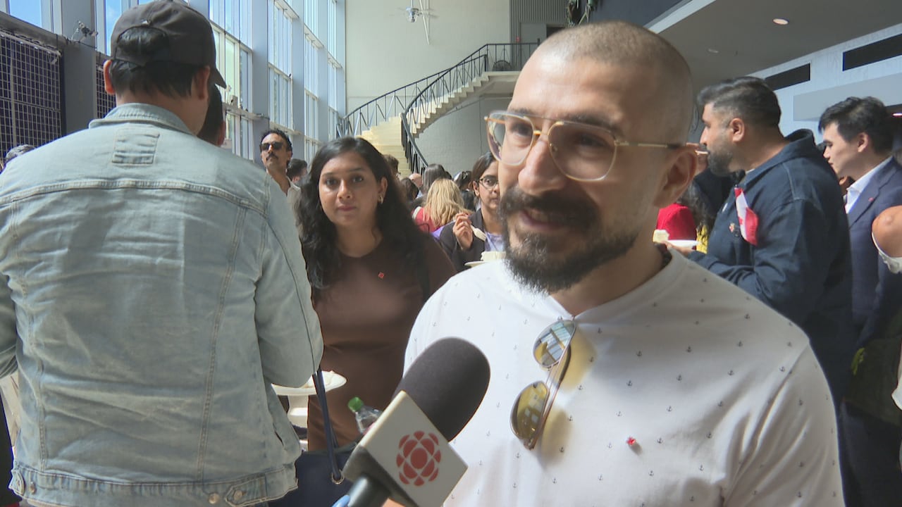 A man in a white shirt and glasses speaks into a CBC microphone.