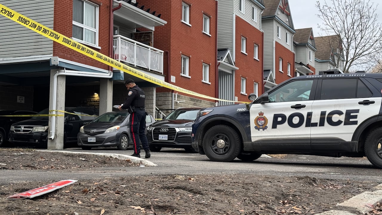 A townhome seen in the early morning. Police tape stretches across the driveway and an officer and parked police car are visible.