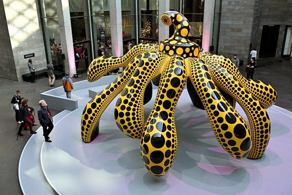 A large yellow and black art sculpture is shown on a pedestal at a gallery.