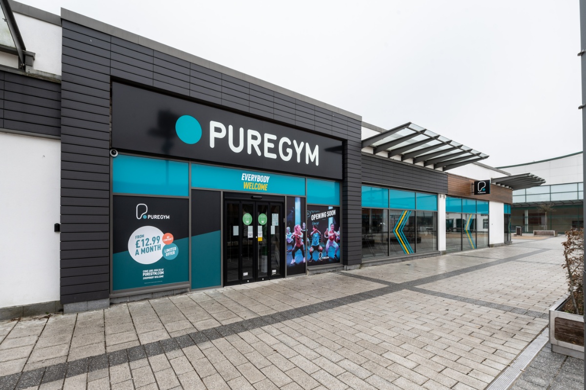 Exterior view of PureGym Aldershot, a modern fitness center with large windows and promotional signage