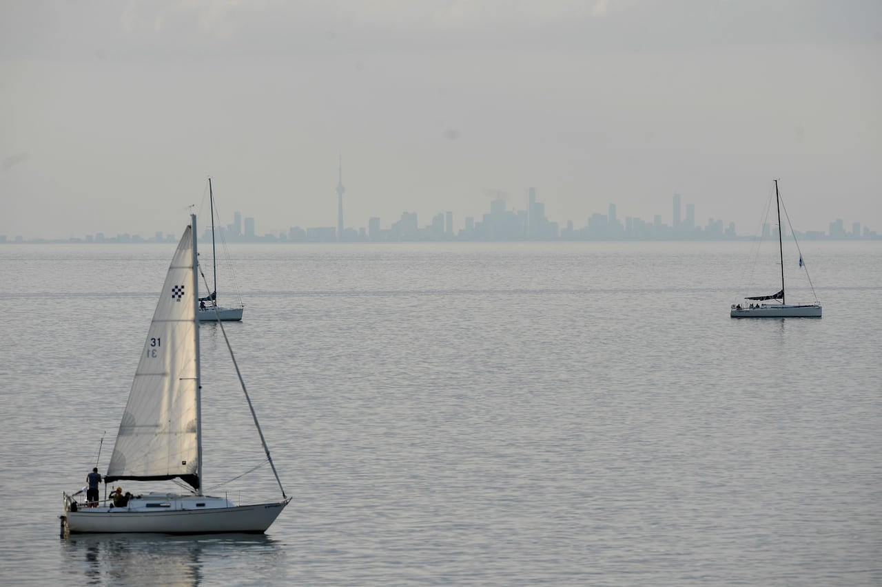 Boats are seen in a body of water as a city skyline is seen in the background.