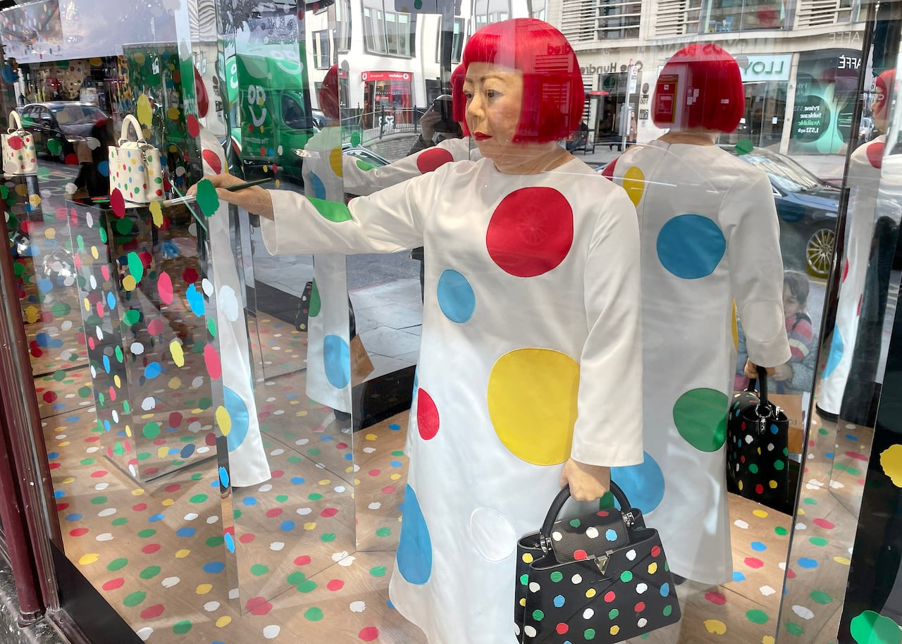 A sculpture of Yayoi Kusama holding a Louis Vuitton bag in a shop window