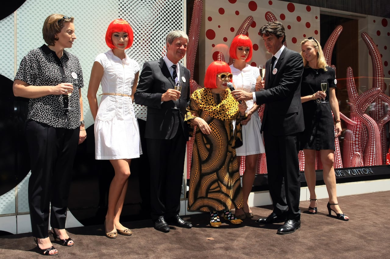 a picture of Yayoi Kusama surrounded by executives from Louis Vuitton