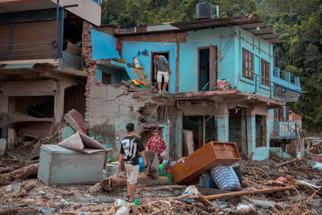 People mill around in a muddy area with destroyed buildings.