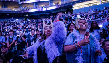 two women in headdresses cheer in stadium with blue and purple light
