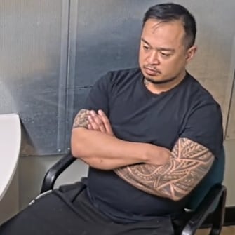 A man with tattoos on his arms cross his arms while sitting in a office chair