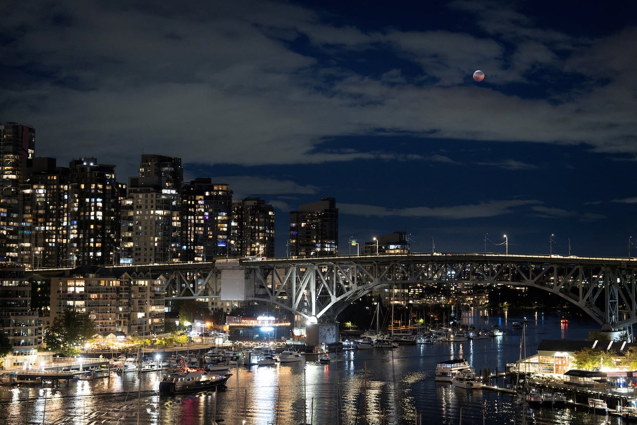 Condos and a bridge lit at night, with a rising full moon in the sky.