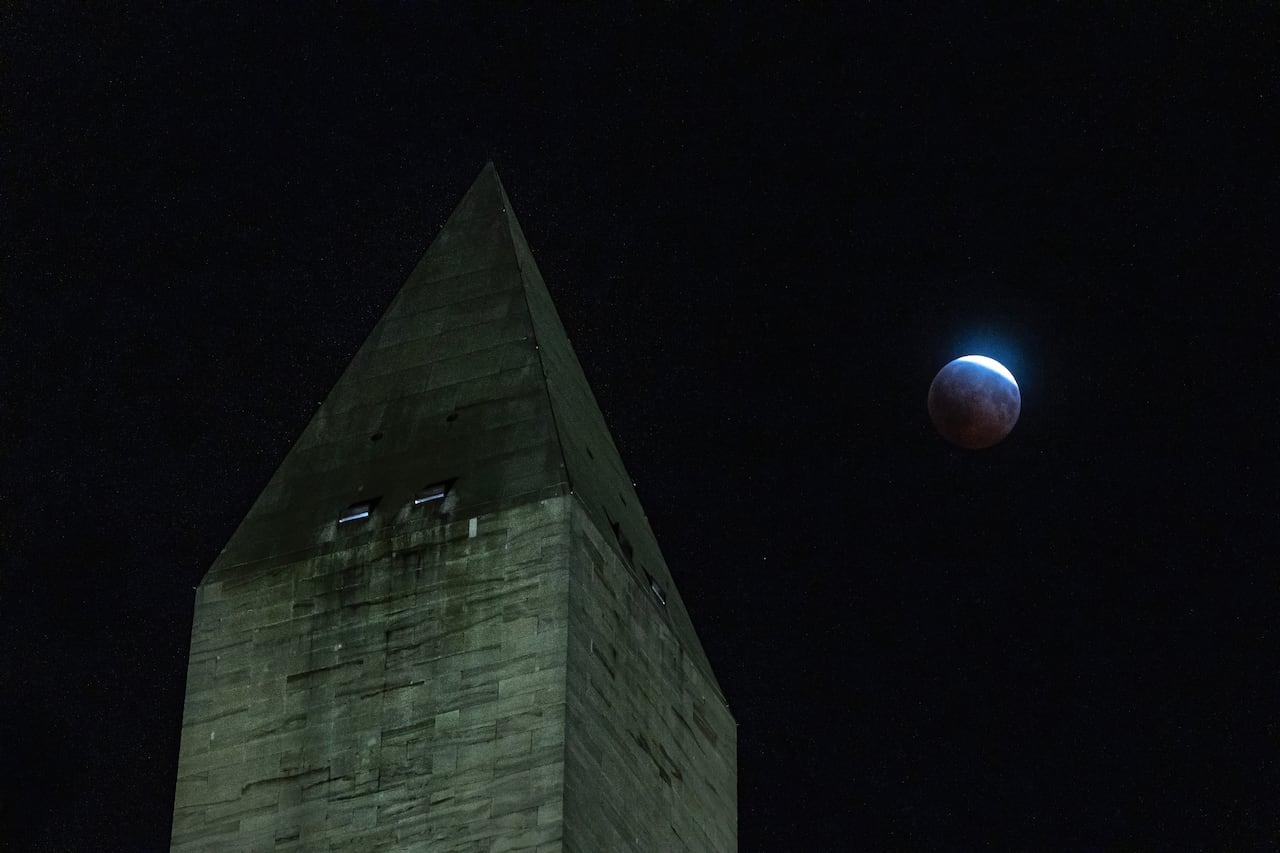 A partial lunar eclipse is seen rising behind an obelisk.