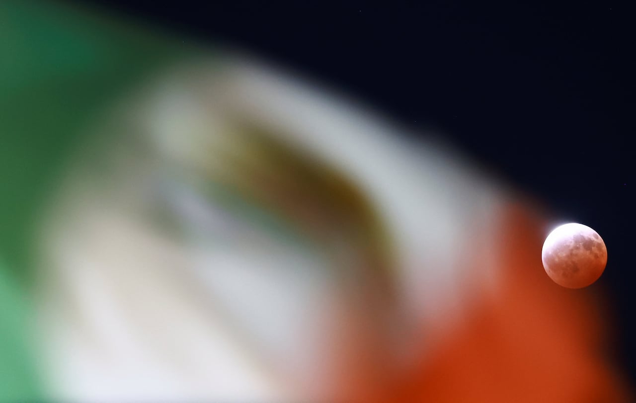 A full moon during a partial lunar eclipse with blurry Mexican national flag in the foreground.