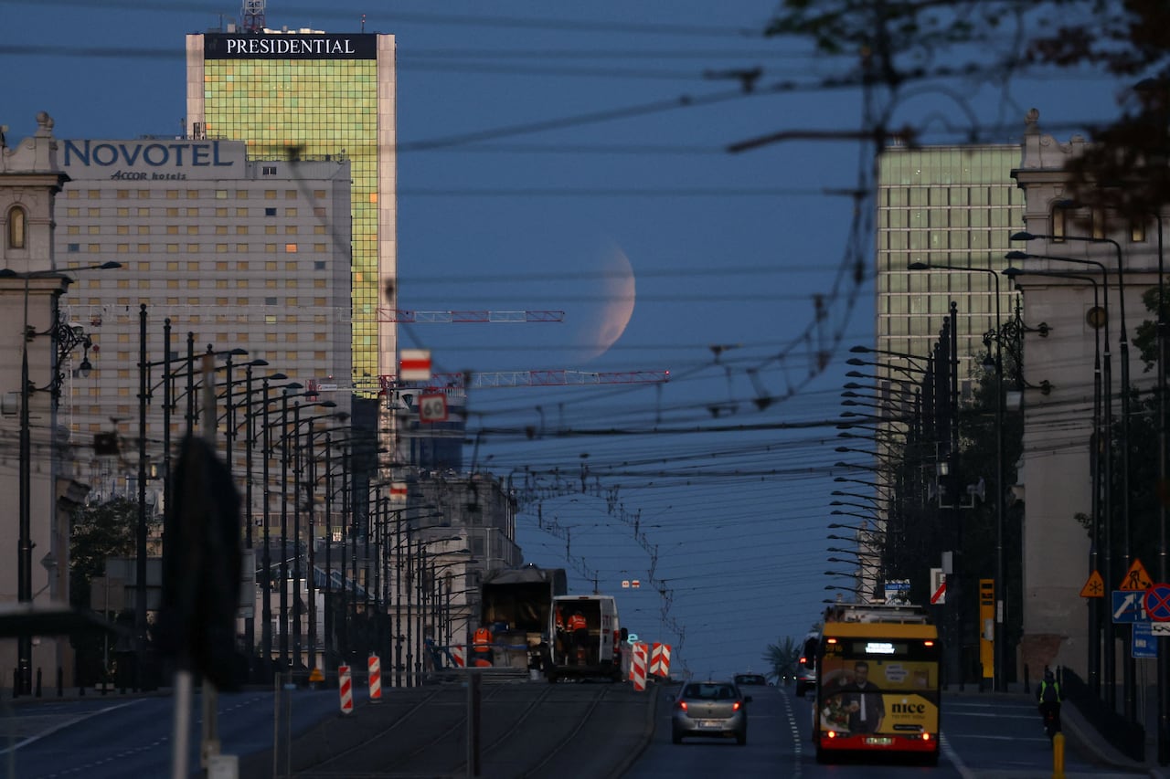 A full moon rising over street flanked by buildings.