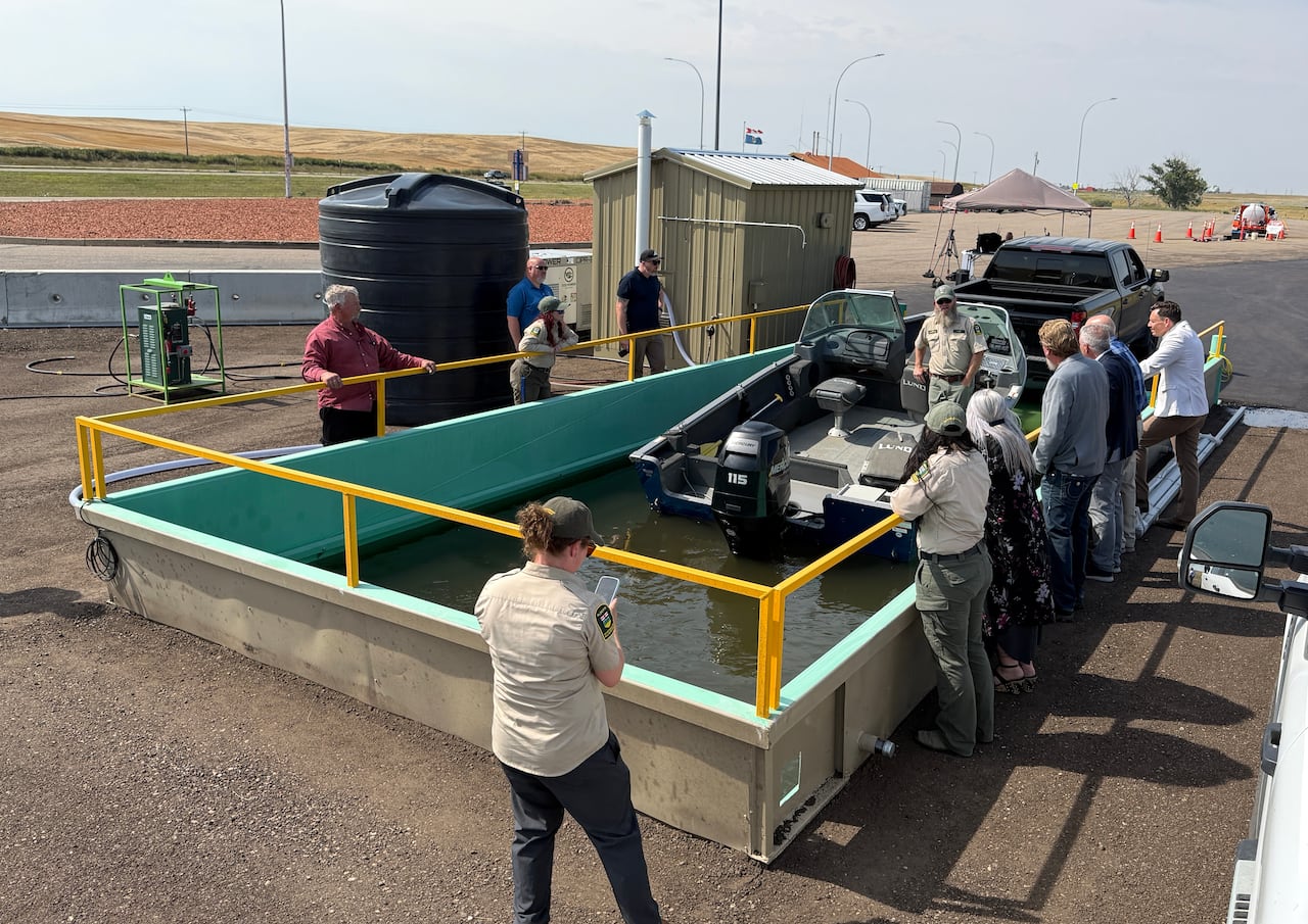 People ring a the railing around a concrete basing filled with green water. A motorboat is sitting in the water.