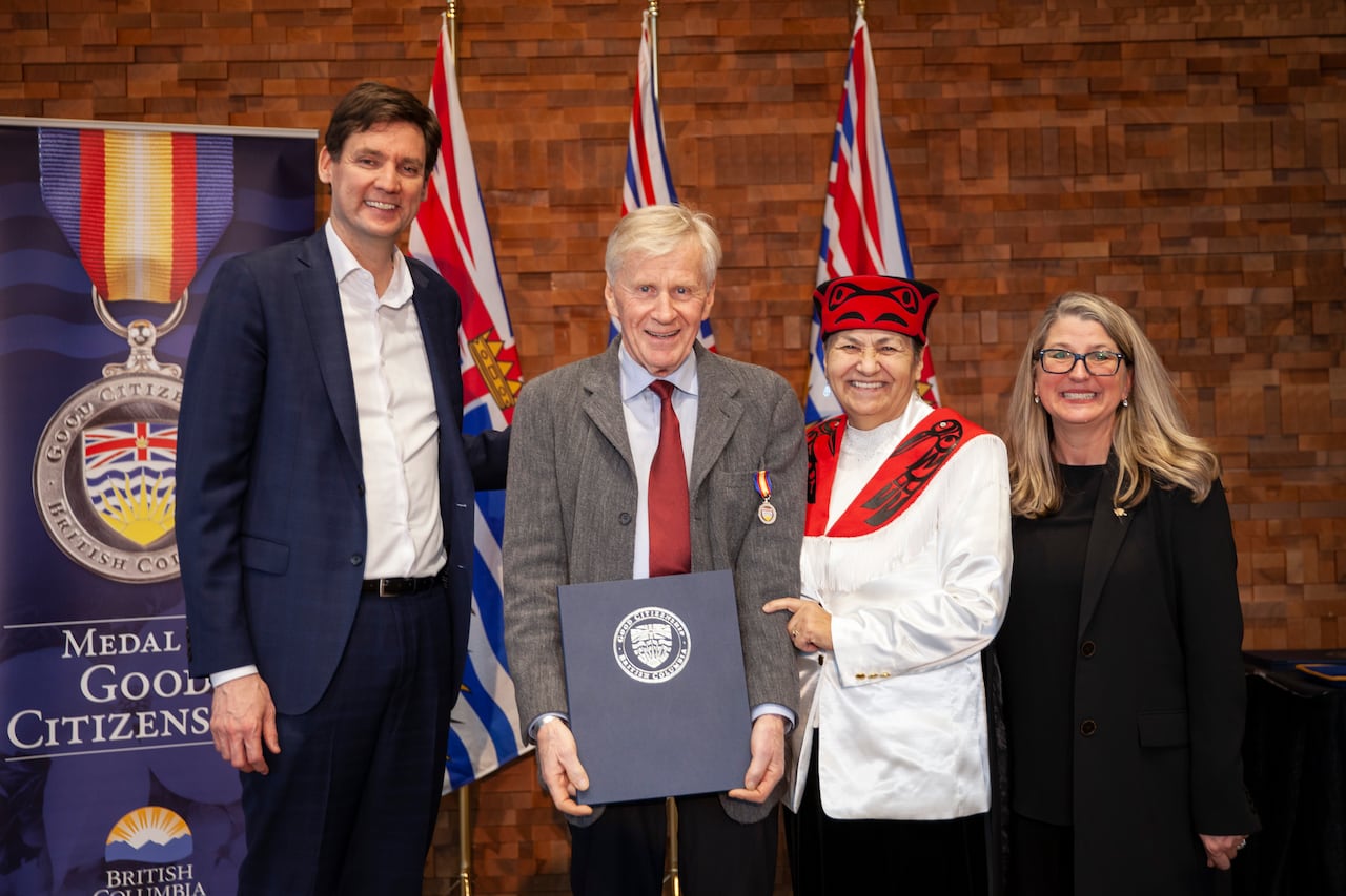 A tall white man, an Indigenous woman and a blond woman smile as they present a certificate to a smiling older man.