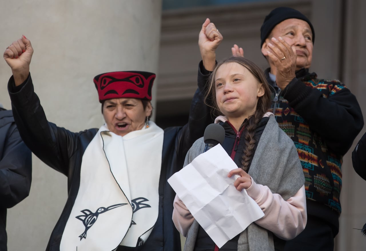 A woman raises her hand in celebration behind a teenage girl, with an older man next to her.