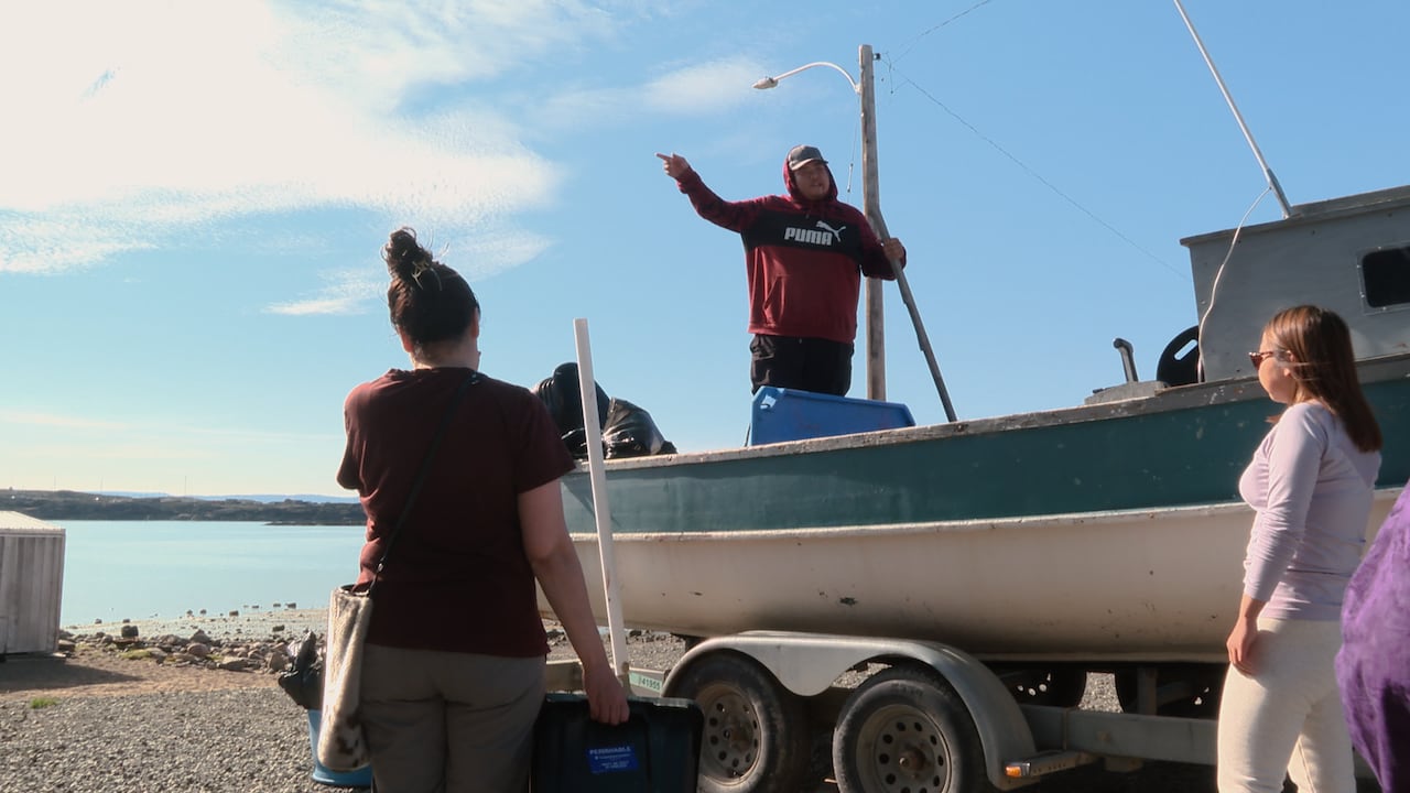 Man stands on boat, speaking to people on land.