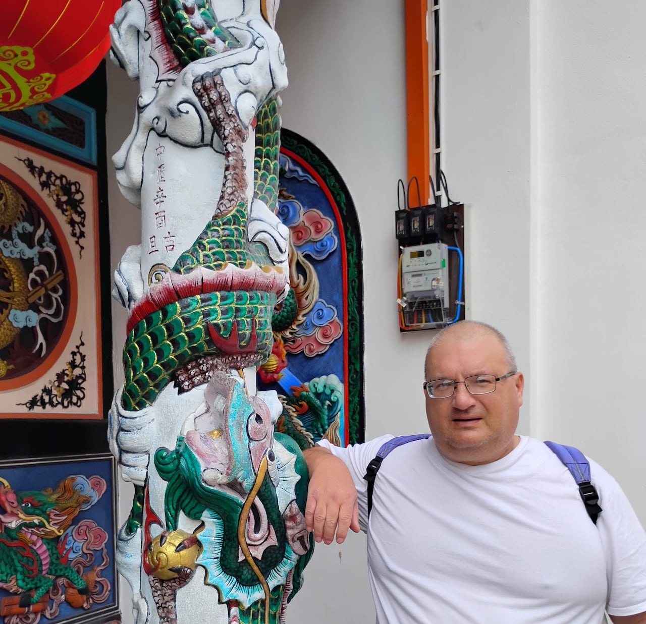 A man wearing glasses stands next to Chinese art.