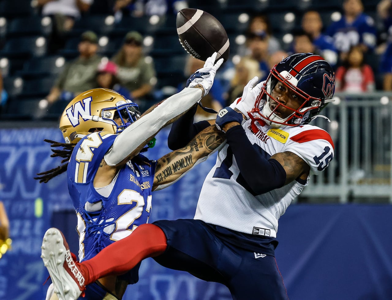 A football player wearing blue and gold knocks the ball out of the hands of another football player wearing white, red and navy blue