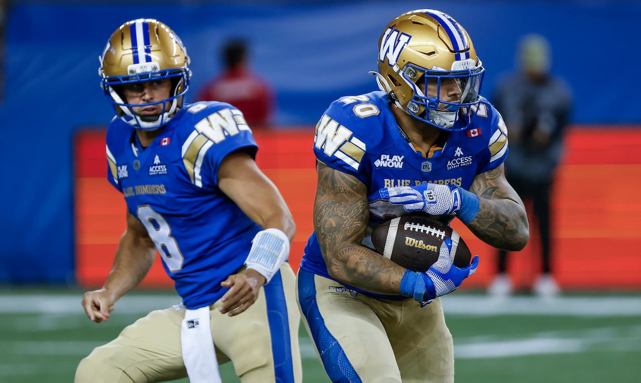 Two football players wearing blue, gold and white jerseys. One player starts to cradle a football and run