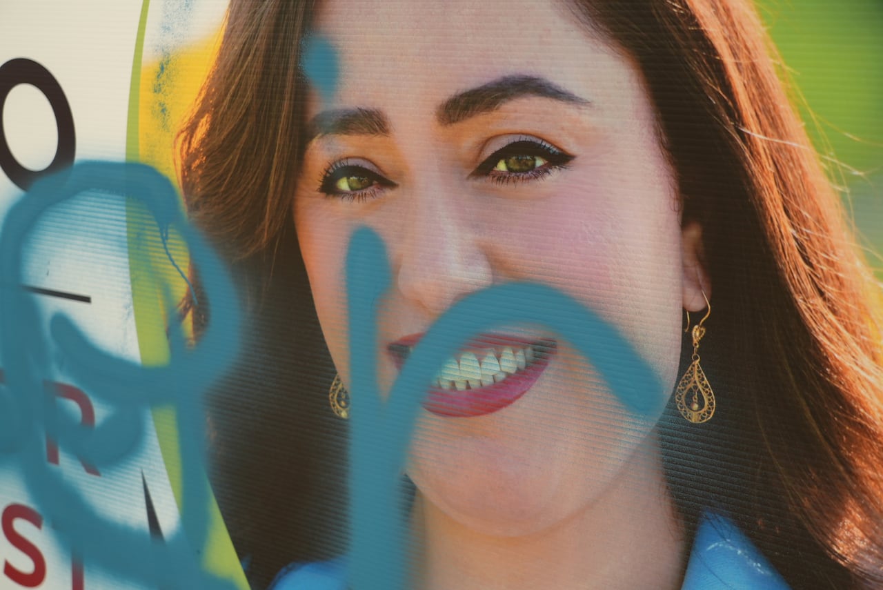 A close up shot of a campaign sign showing the candidates face defaced with blue spray paint.