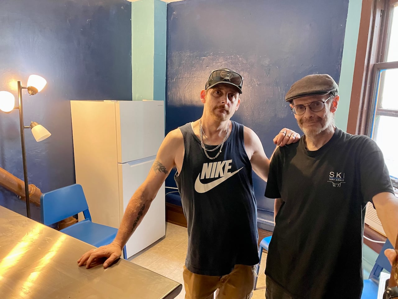 Two men pose in a room with blue walls.