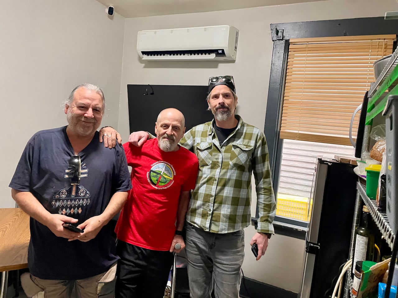 Three men pose for a photo in a room with a heat pump visible in the background.
