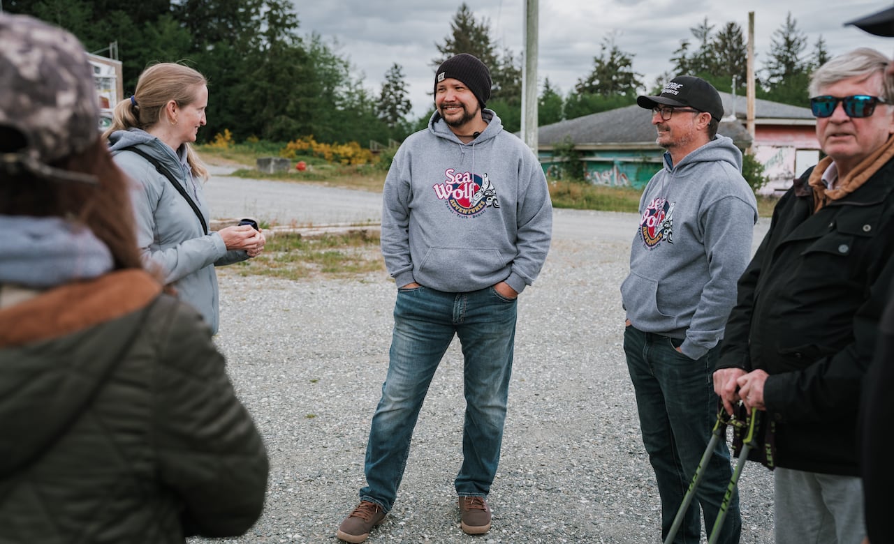 Two men wearing grey hoodies smile near others in an outdoor environment.