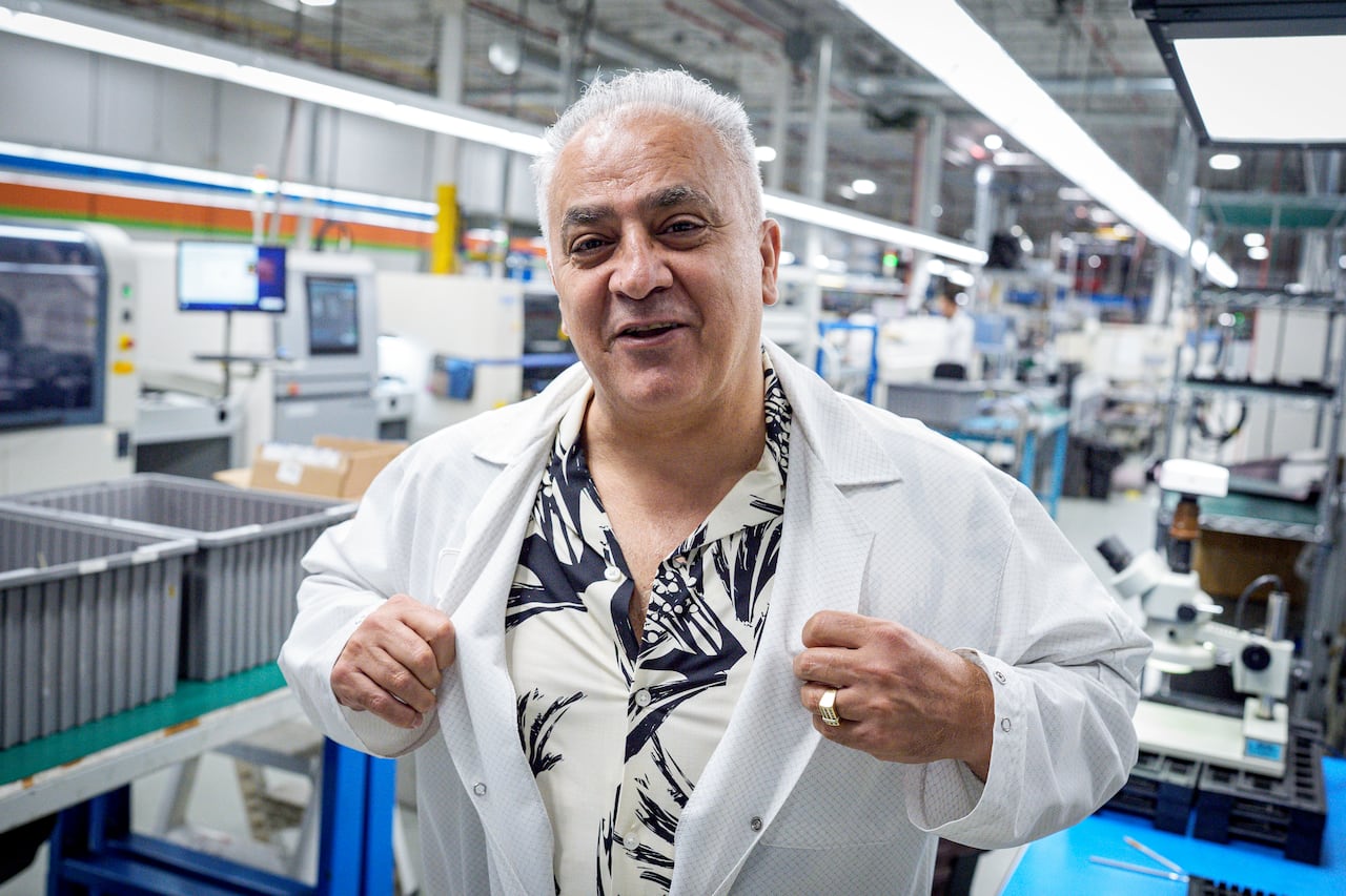 A man putting on a white lab coat at a manufacturing plant of printed circuit boards.