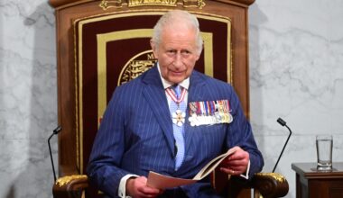 King Charles on a throne-like chair, wearing medals and holding an open book.