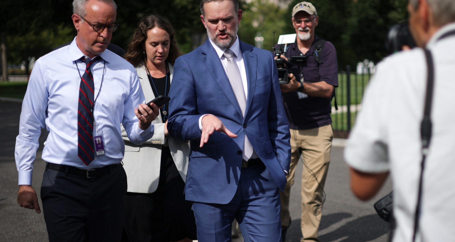 Jamieson Greer walks outside while speaking to journalists and surrounded by cameras.