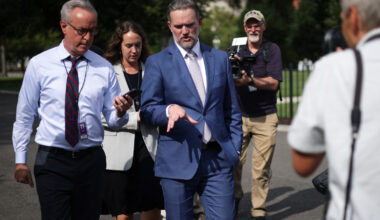 Jamieson Greer walks outside while speaking to journalists and surrounded by cameras.