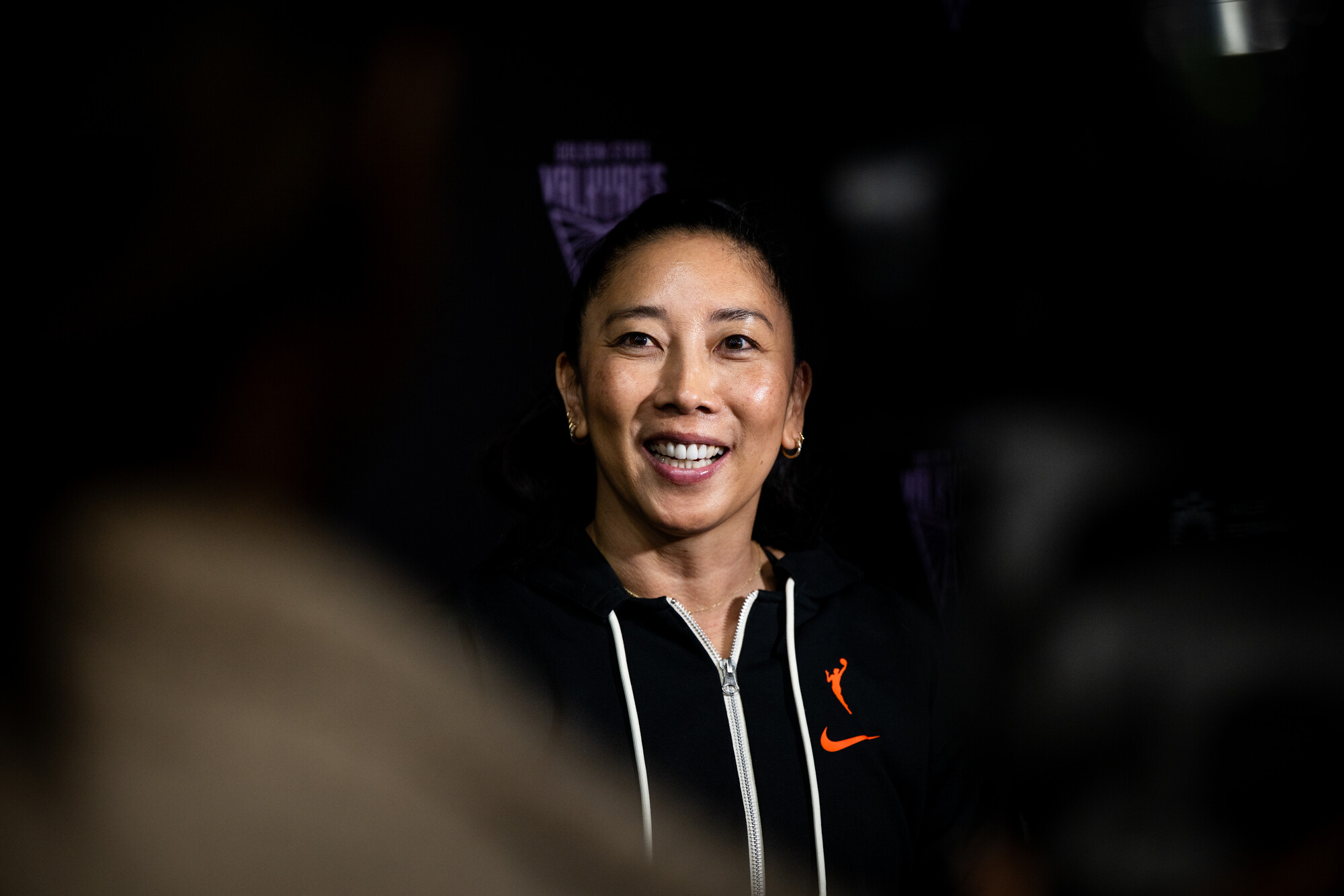Asian woman smiles in black hoodie during press coference