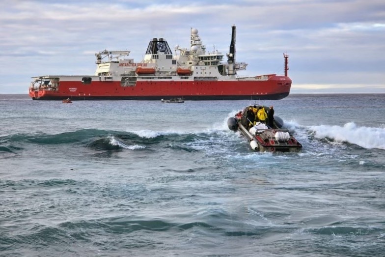 A small boat heads towards a larger red ship in the distance.