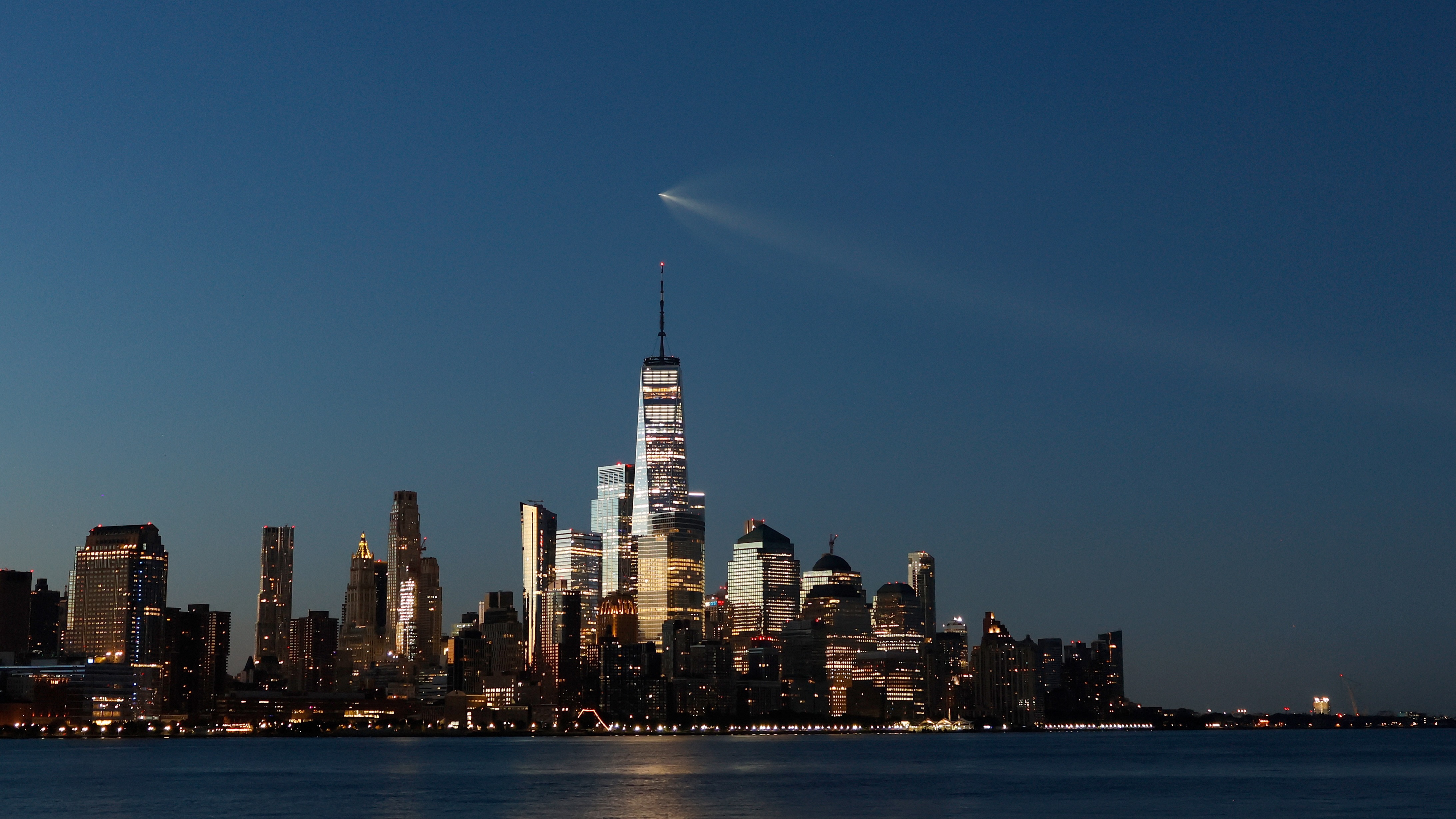 long-distance photo of a rocket cruising over the New York City skyline shortly before dawn. the rocket looks kind of like a comet