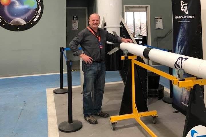 A man stands next to a rocket, with his hand resting on it.