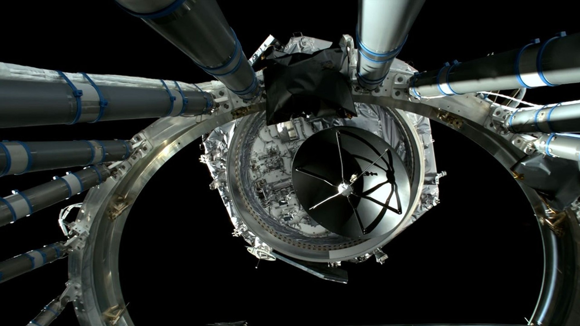 a hexagonal spacecraft floats away from a large metal ring on a black background