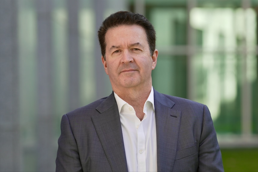 A man in a grey suit and white shirt looking toward the camera.