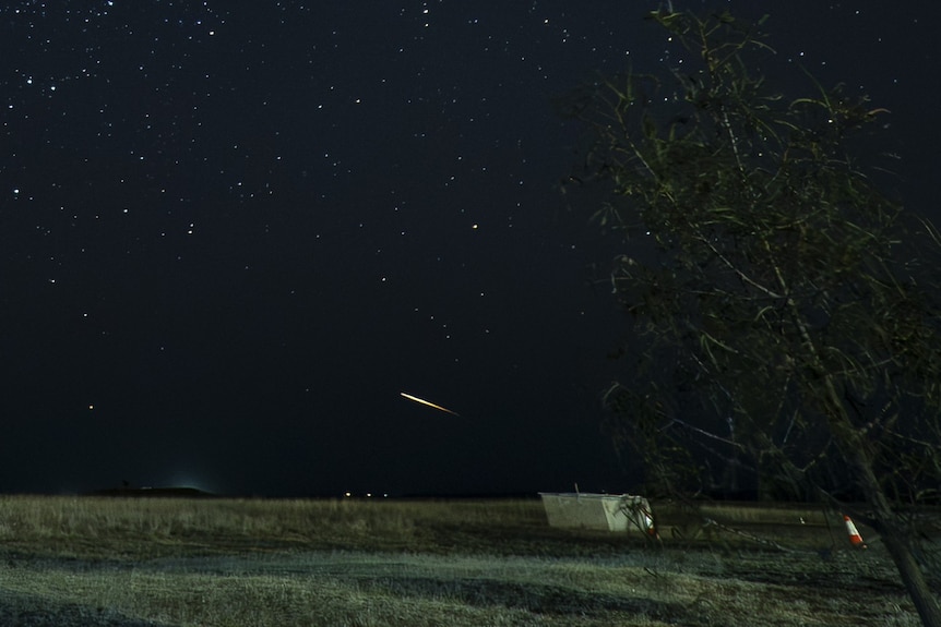 A small streak of light is seen above a field at night.