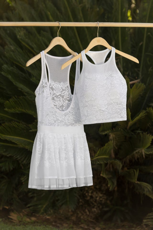 Two white lace garments hanging on wooden hangers against a green background.